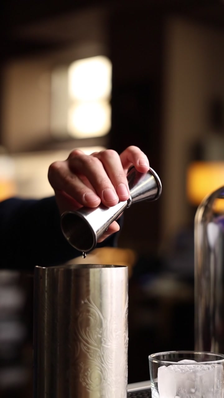 Barman sirviendo líquido de un jigger en una coctelera