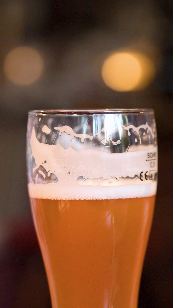 Primo piano di un bicchiere da pinta di birra artigianale ambrata con schiuma, illuminazione calda, bassa profondità di campo