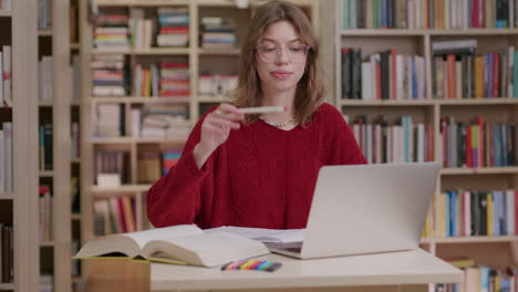 mujer joven en la biblioteca investigando con laptop y libros