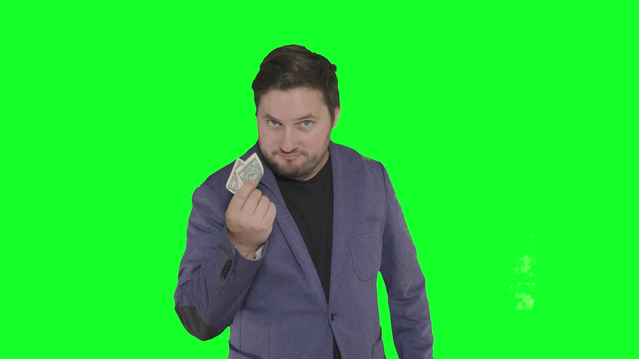 Skäggig kaukasisk skådespelare som leker med papperspengar framför kameran med alfabakgrund på green screen.