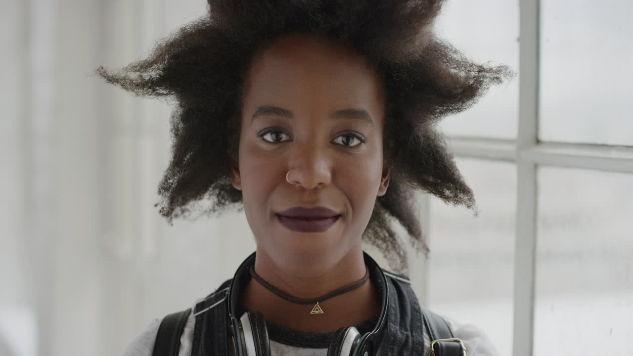 retrato de una mujer afroamericana segura de sí misma sonriendo con calma mirando a la cámara joven estudiante con un peinado afro funky en el fondo del apartamento serie de personas reales