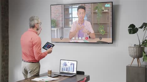 hombre de negocios caucásico en videollamada con un colega caucásico en la pantalla de televisión