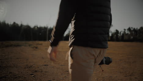 Tracking-arc-shot-of-a-young-millennial-professional-photographer-or-travel-blogger-walking-out-in-nature-at-sunset-with-his-DSLR-mirrorless-camera-and-lens-to-capture-photos-of-his-travel-adventures