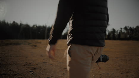 tracking arc shot of a young millennial professional photographer or travel blogger walking out in nature at sunset with his dslr mirrorless camera and lens to capture photos of his travel adventures