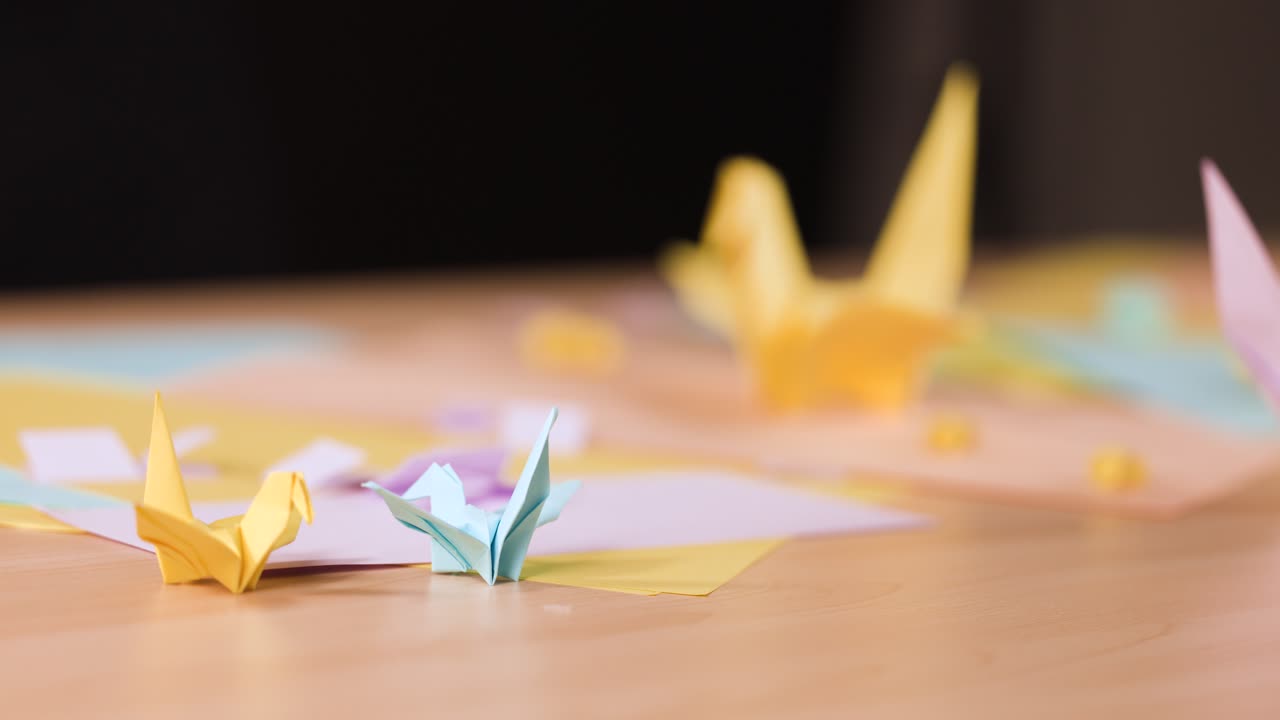 Primo piano di mani che posizionano una gru di carta rosa tra altri uccelli origami colorati