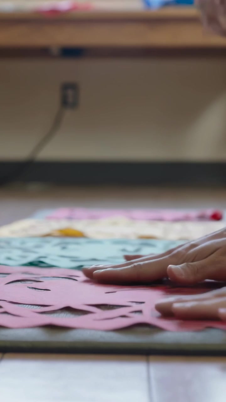Vertical video: Smoothing hands reaching in, aligning red pink teal paper in craft room, making art