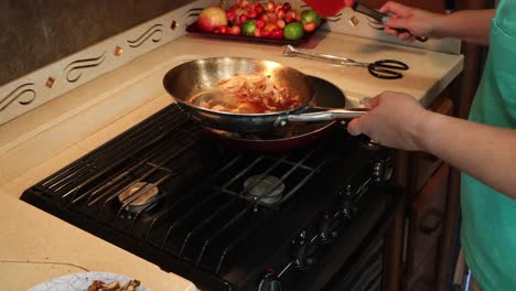 Frau,-Die-Gekochtes-Steak-Und-Zwiebeln-In-Eine-Andere-Pfanne-Schiebt,-Gebratene-Kartoffeln-Aus-Dem-Ofen-Nimmt-Und-Die-Kartoffeln-Anrichtet