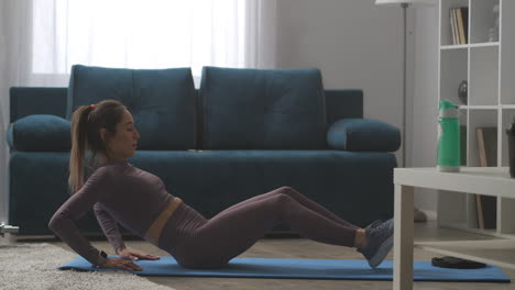 modelo de fitness está haciendo abdominales para el abdomen delgado en casa sentado en el suelo y levantando el torso y las piernas mujer deportiva activa ejercicio físico para la formación del cuerpo