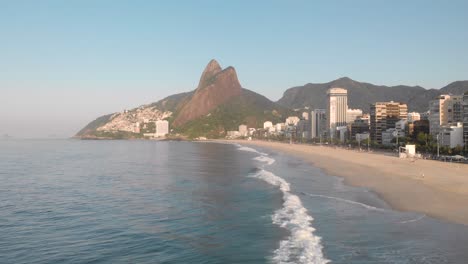 respaldo aéreo sobre las olas del océano con vistas a la playa de la ciudad costera de río de janeiro durante la hora dorada de la madrugada