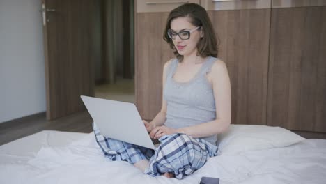 woman in pajamas using laptop in bedroom