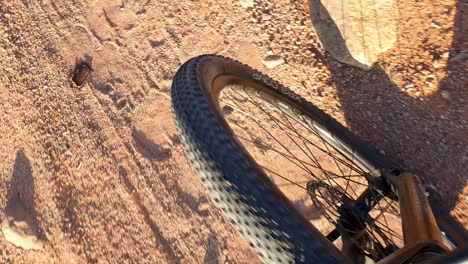 Top-down-view-of-front-wheel-of-mountain-bike-cycling-through-remote,-rough-and-bumpy-red-sandy-desert-terrain-during-adventure