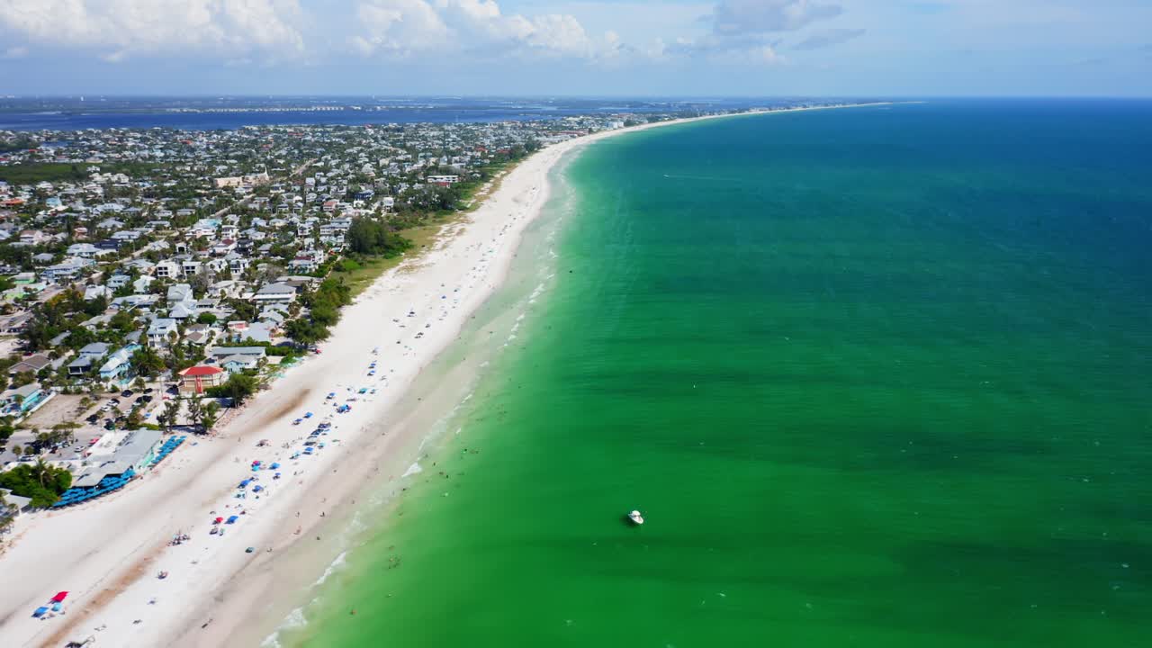 Anna Maria Island’s coastline stretches in a sweeping curve of turquoise Gulf water and soft white sand, lined with colorful seaside homes under bright summer light