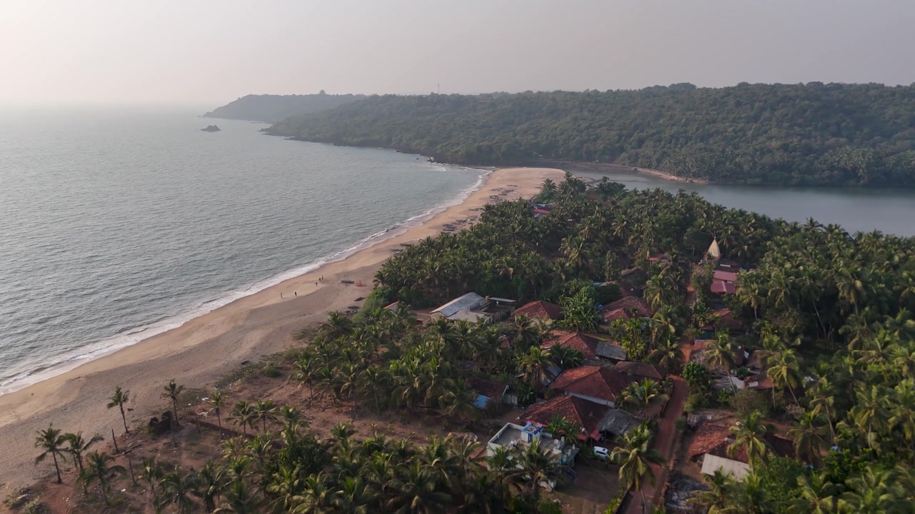 High-angle aerial view of a traditional fishing village on a sandbar between the ocean and a river at Kelus Kalvi Beach, India.