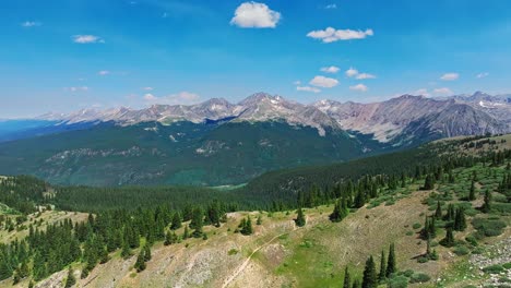 Antena-Sobre-Los-árboles-Y-Colinas-De-Cottonwood-Pass-Con-Las-Montañas-Rocosas-En-El-Fondo,-Colorado,-EE.UU.