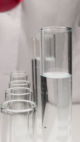 student in white robe replaces test tubes on rack in laboratory slow motion. probe lens shot of chemical researching work extreme closeup