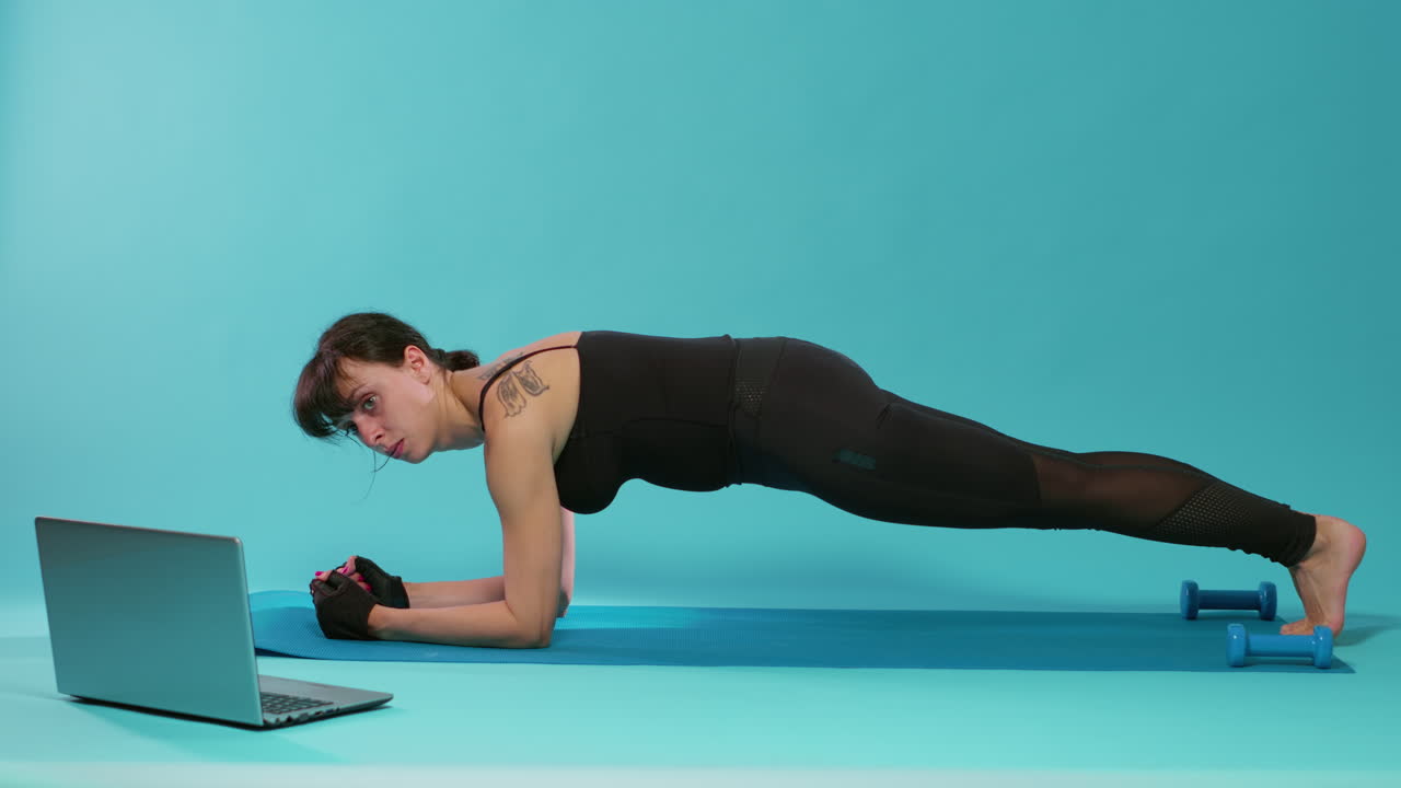 Athete sitting in plank position on yoga mat over blue background