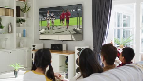 Composite-of-happy-family-sitting-at-home-together-watching-rugby-match-on-tv