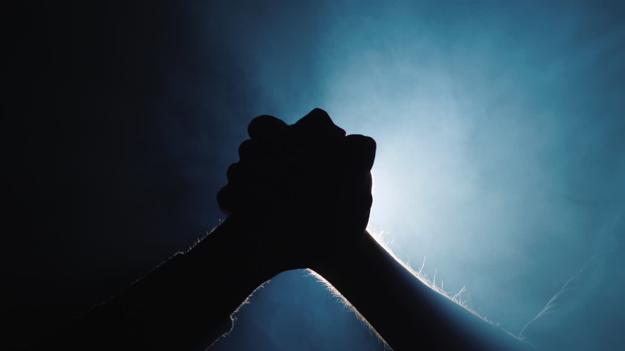 두 손이 연기와 빛의 광선을 배경으로 팔씨름을 하고 있다