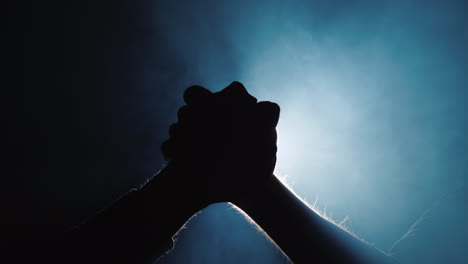 two hands fight in arm wrestling against the background of smoke and rays of light