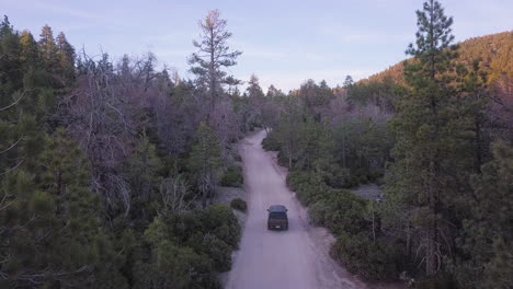 4wd vehicle driving through forest mountain road, rising aerial reveal