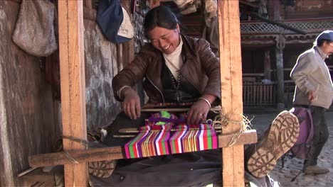 a woman operates a basic loom in a chinese village