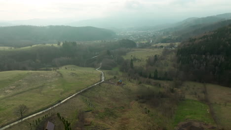 A-secluded-wooden-house-nestles-in-a-mountain-valley-with-a-meandering-path-leading-towards-a-distant-town-amidst-forested-hills