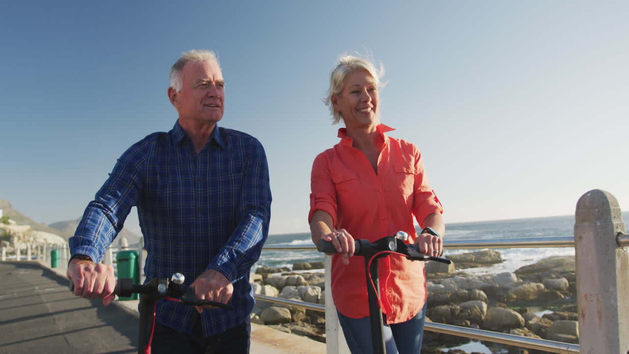 Senior couple walking next to electronic scooter alongside beach