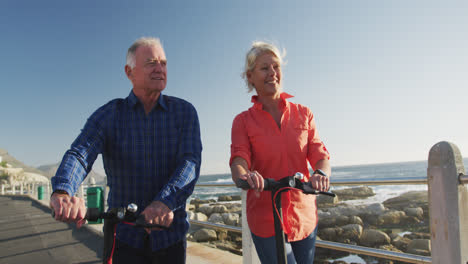 senior couple walking next to electronic scooter alongside beach