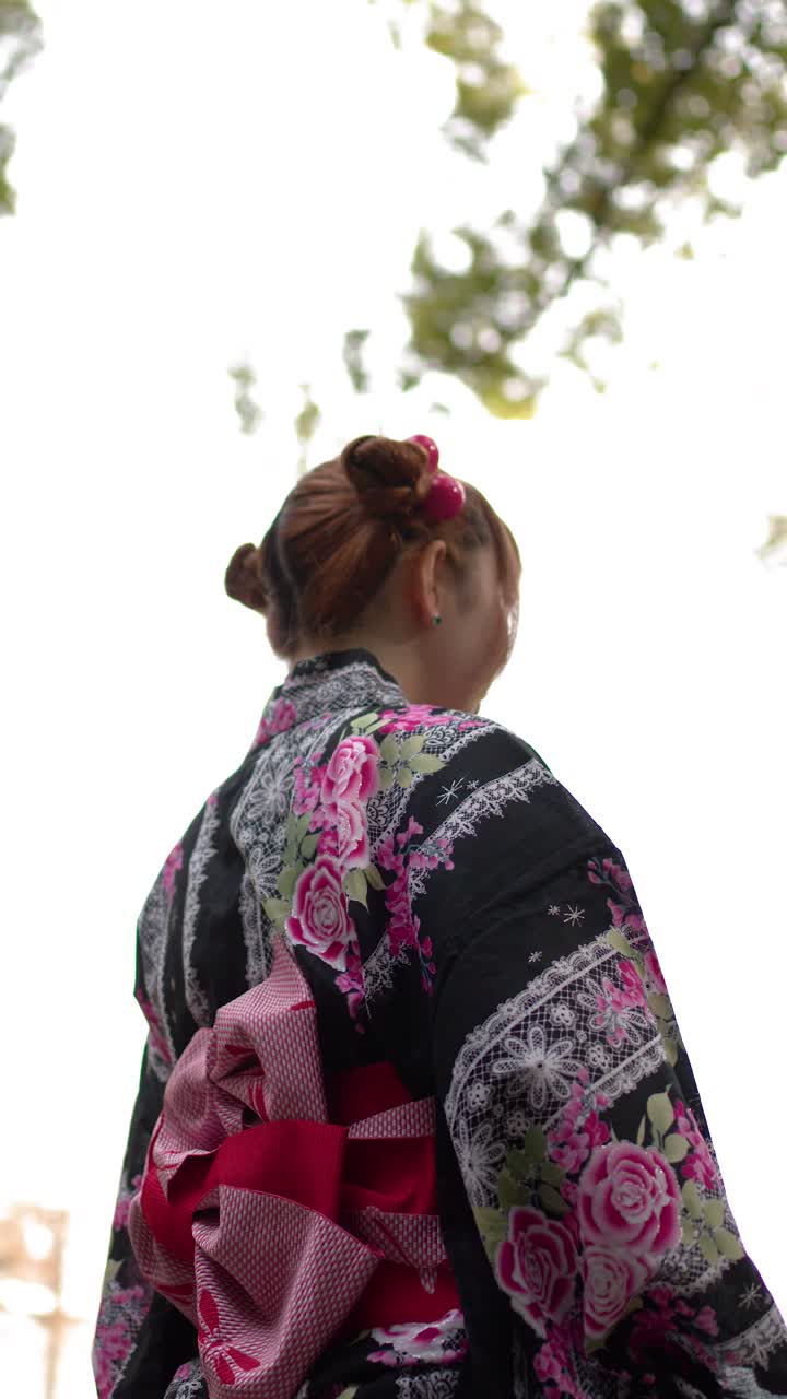 Uma mulher vestindo um yukata tradicional caminha entre as árvores em um templo xintoísta em Tóquio.