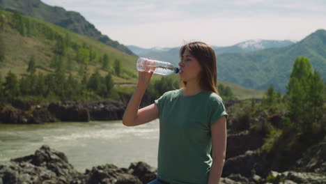 pretty woman refreshes drinking water on rocky riverbank