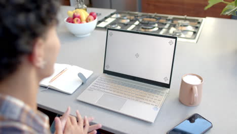 using laptop on kitchen counter, teenage boy gesturing with notebook and coffee nearby, copy space