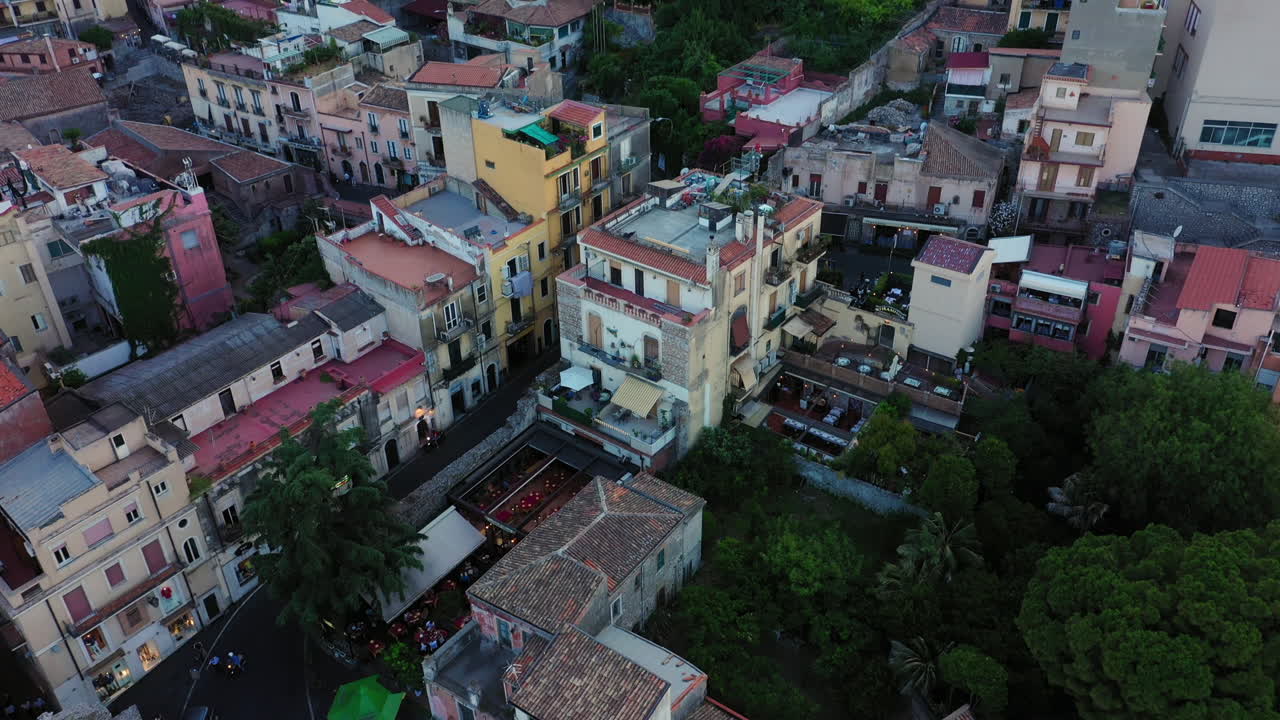 Aerial shot of the medieval buildings in Sicilian commune; Taormina, Italy. Camera goes down and tilts up to reveal a mountain above the city