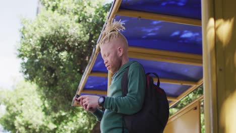 thoughtful albino african american man with dreadlocks using smartphone