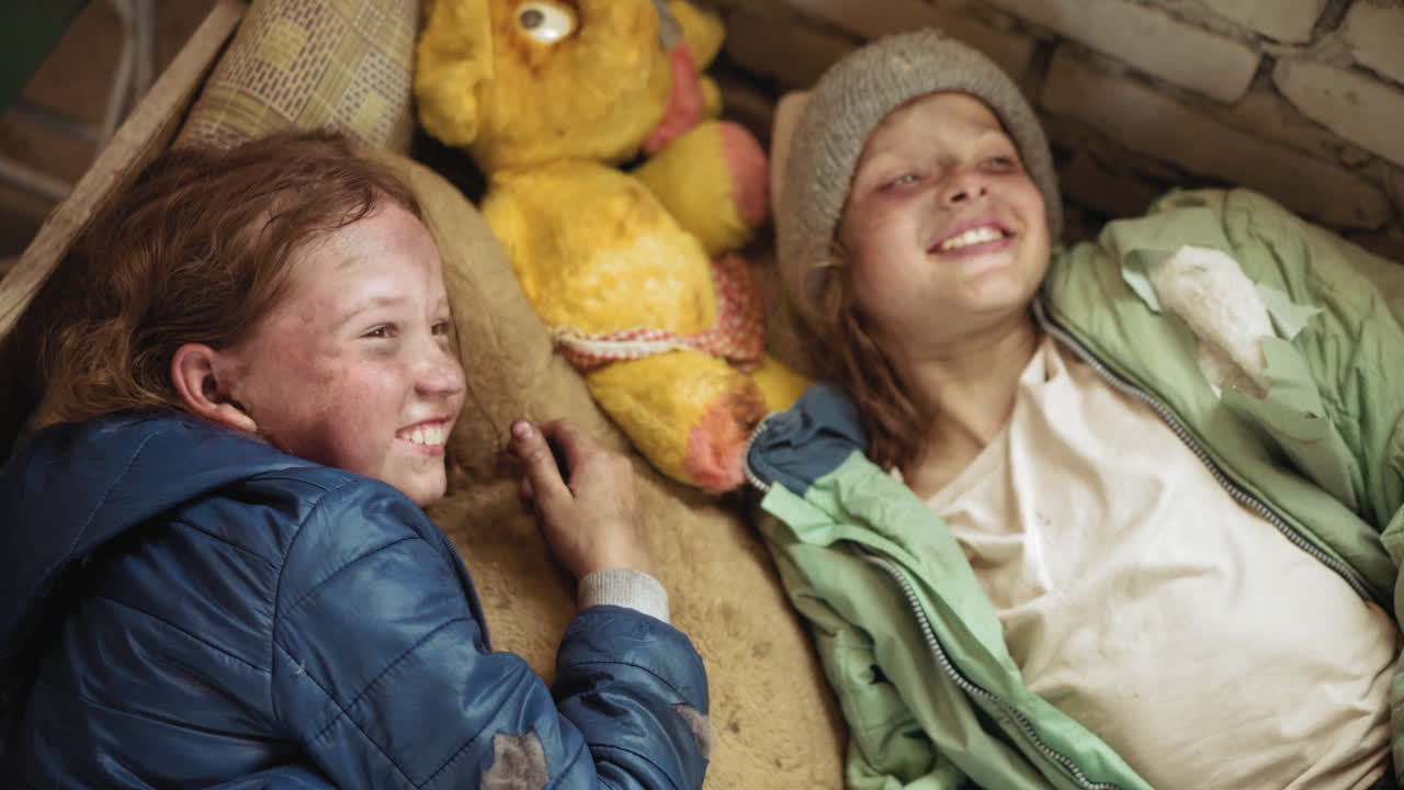 낡은 매트리스 위에 낡은 인형을 사이에 두고 누워 서로 따뜻한 눈빛을 나누는 버려진 아이들, 흙먼지가 묻었지만 희미한 미소로 부드러워진 얼굴, 찢어진 재킷과 거친 벽