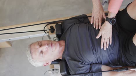 focused senior caucasian man using reformer with female pilates coach, unaltered, in slow motion