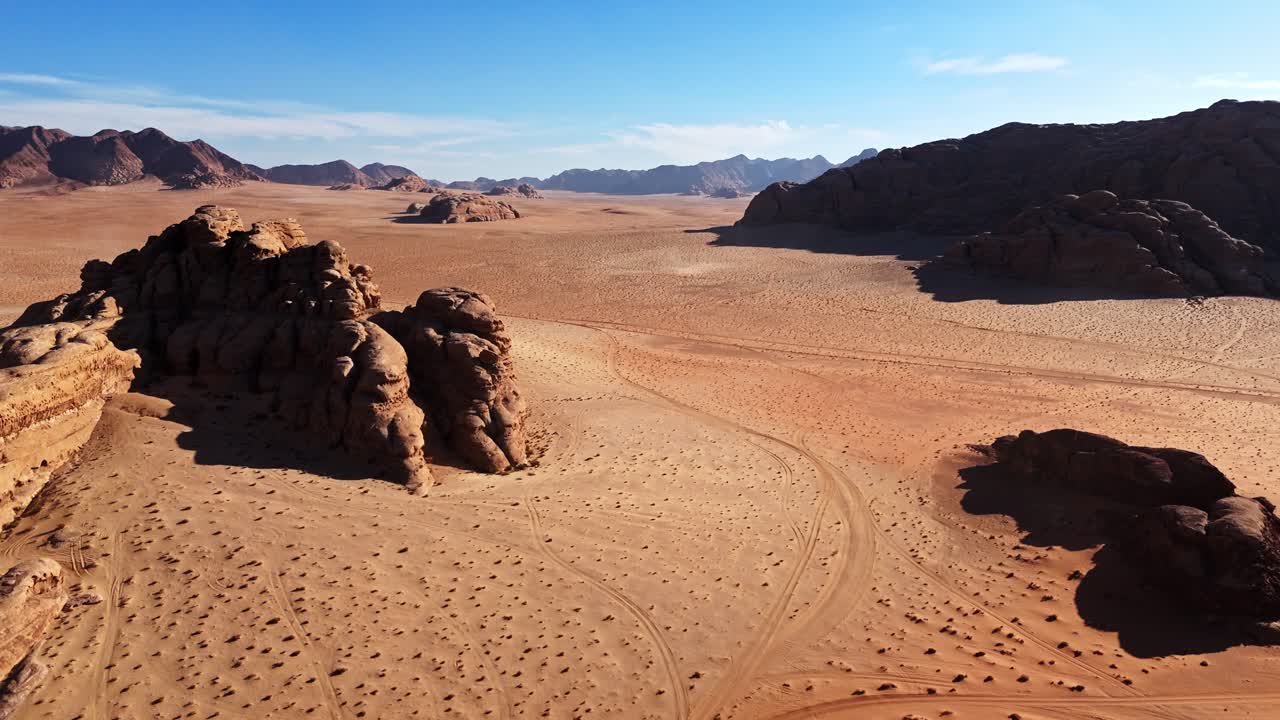 Prospettiva aerea di una valle desertica a Wadi Rum, in Giordania, con intricate tracce di pneumatici sulla sabbia arancione e maestose montagne di arenaria sotto un cielo limpido