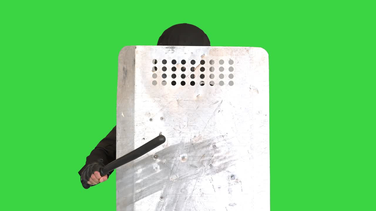 Special unit policeman covering with a shield and holding a baton on a Green Screen, Chroma Key