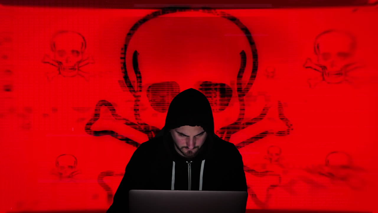 un hacker encapuchado negro programa un virus informático frente a un enorme símbolo verde de calavera y tibias cruzadas
