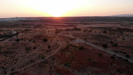 Drone-Aterrizando-En-El-Desierto-Durante-La-Puesta-De-Sol-Con-Un-Coche-Pasando-En-El-Fondo-En-Albufeira,-Portugal