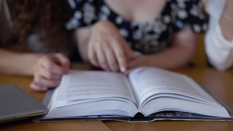 tres estudiantes leyendo un libro juntos en la biblioteca, señalando el texto