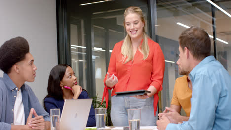 Feliz-Mujer-De-Negocios-Caucásica-Casual-Con-Tableta-Hablando-Con-Diversos-Colegas-En-Una-Reunión-De-Oficina