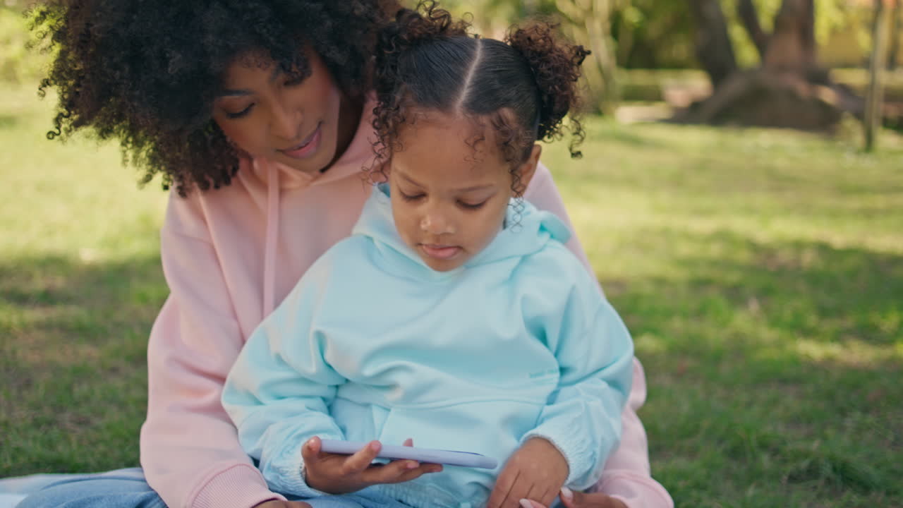 Child watching entertaining video with mother on nature picnic weekend close up.