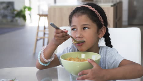 Ein-Mädchen-Mit-Gemischter-Abstammung-Genießt-Eine-Schüssel-Müsli-Und-Trägt-Ein-Rosa-Stirnband-Und-Perlenarmbänder.