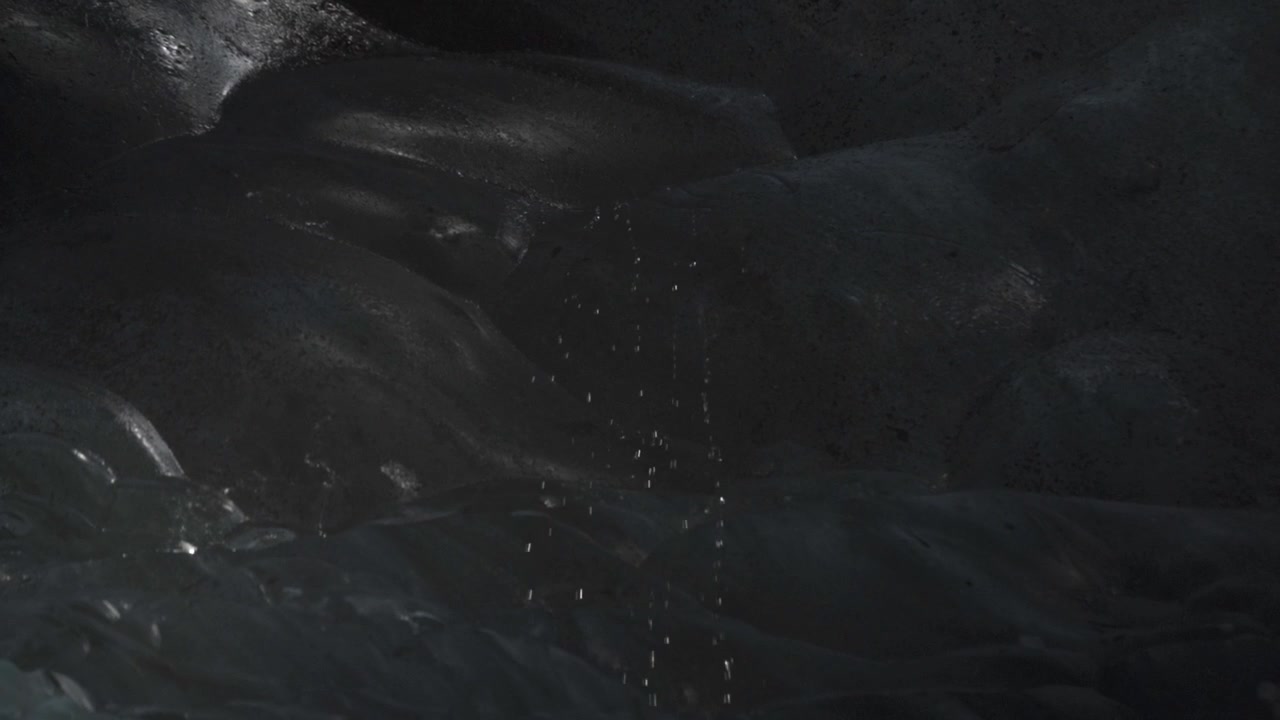 Esplora la sottile bellezza di una grotta di ghiaccio islandese dove delicati rivoli d'acqua scendono lungo le pareti di ghiaccio dalle sfumature blu.