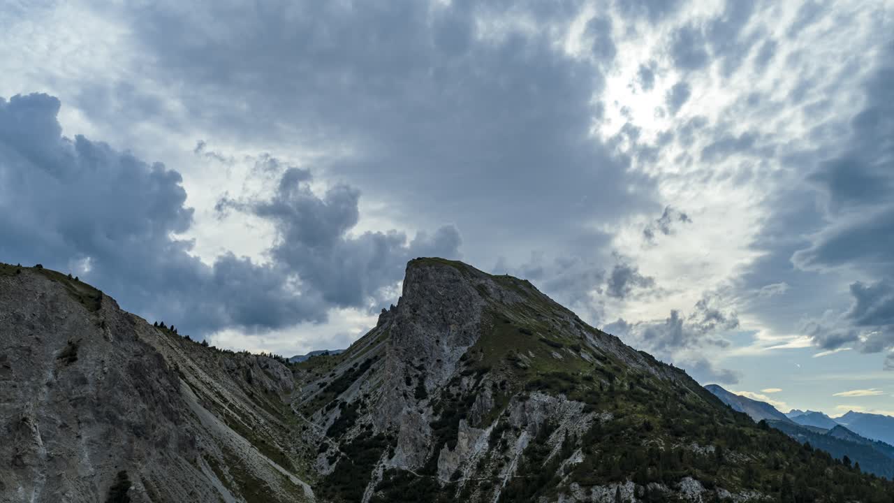 Hyperlapse aereo che mostra il Passo del Fuorn (Ofenpass) nei Grigioni, Svizzera, mettendo in risalto il paesaggio alpino d'alta montagna sotto un cielo nuvoloso con luce solare.