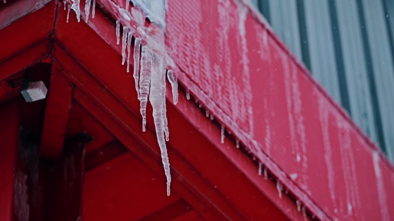 Clear icicles hang from red facade while gentle snow falls in slow motion