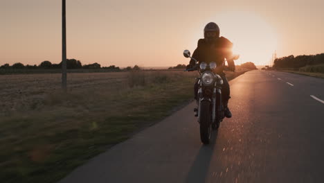 man on a motorcycle riding in the rays of the setting sun on the highway