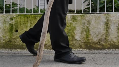 Low-Gimbal-Shot-Of-Elder-Man-Walking-In-Village-With-Wooden-Cane