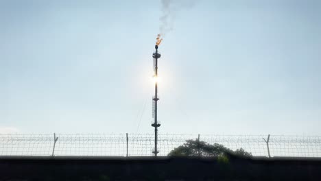 flare pit gas combustion refinery behind wired fence, static, close up, day
