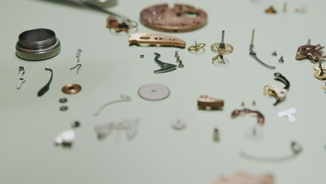 a watchmaker carefully picking up tiny screws using tweezers and placing them into a metal screen container for cleaning - close up